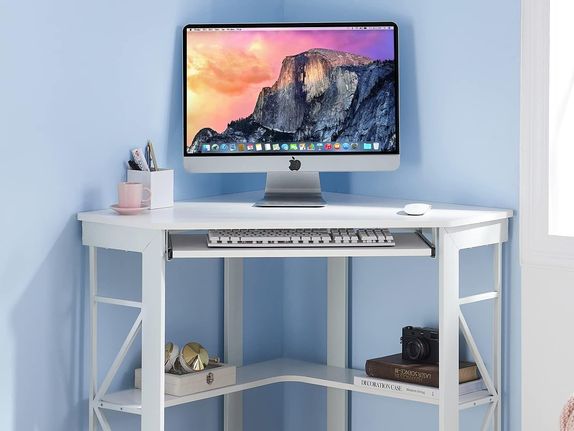 An elegant, small, white corner desk with built in storage and a computer setup on top.