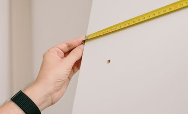 Man measuring wall in a white room.